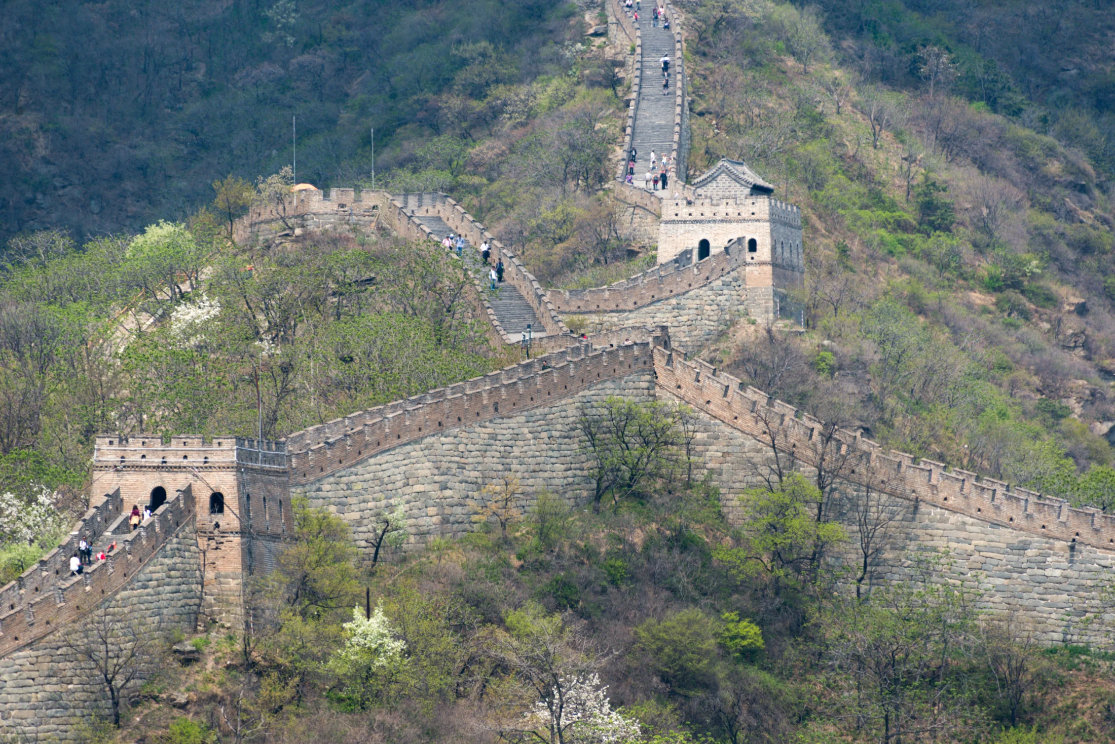 The Great Wall climbs green mountain ridges at Mutianyu with watchtowers and visitors visible along the route.