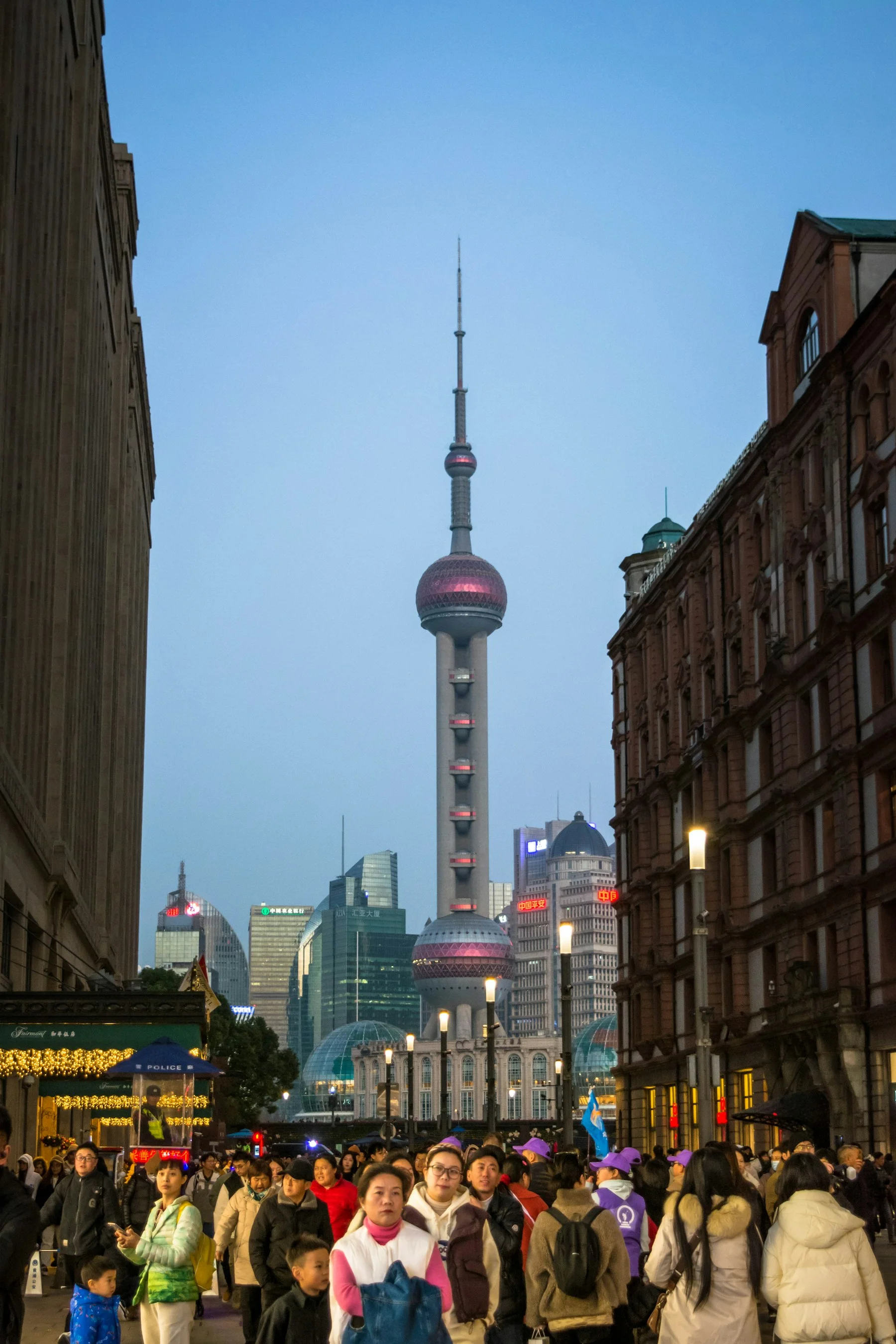 The Oriental Pearl Tower and Pudong skyline appear at blue hour between older buildings along Shanghai's Nanjing Road.
