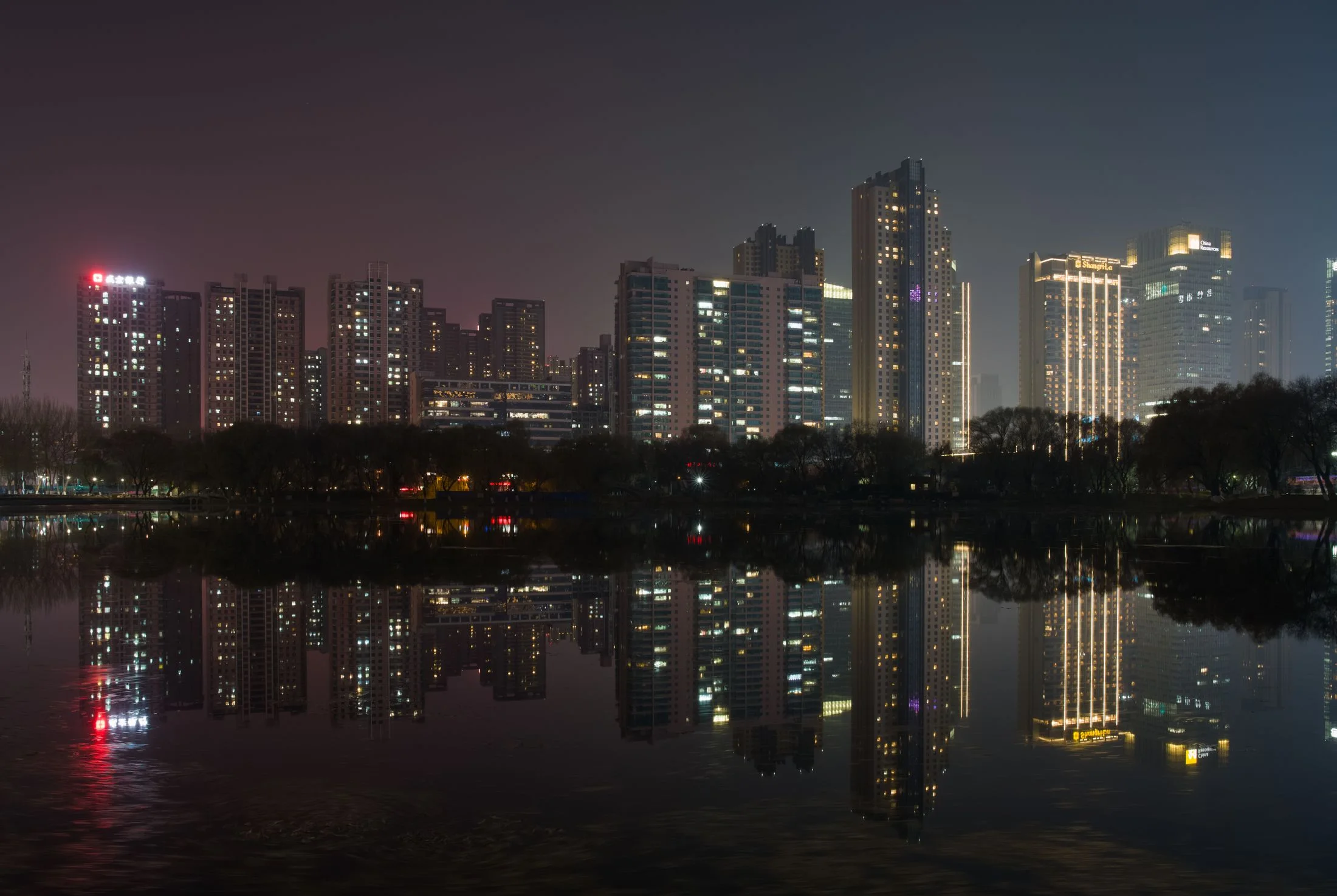 Residential and office towers around Shenyang's Youth Park reflect across the lake on a winter night.