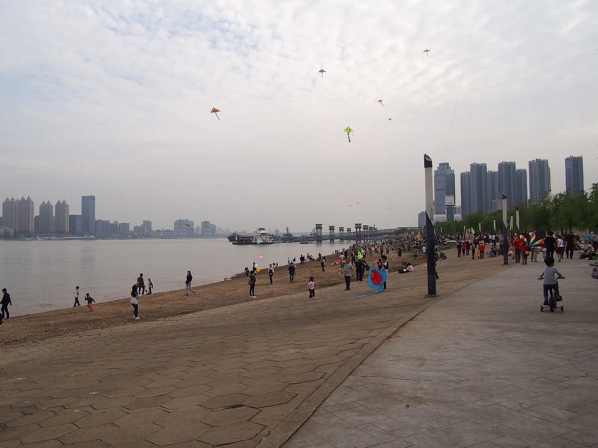 People use the broad Hankou riverfront beside the Yangtze, with the opposite bank and city skyline visible across the water.