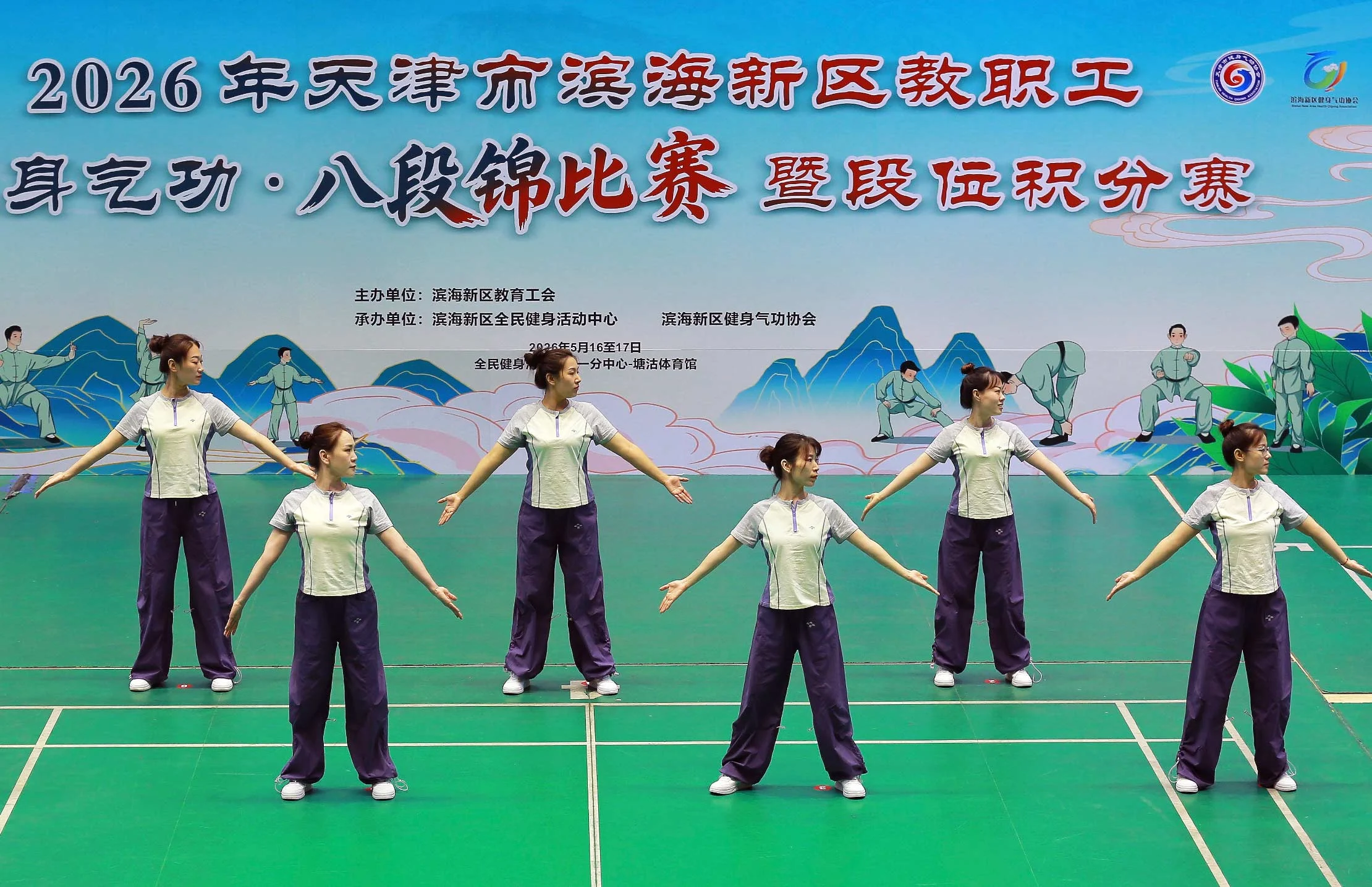 Teachers in coordinated sportswear perform Baduanjin in rows on an indoor court at a 2026 Tianjin Binhai competition.