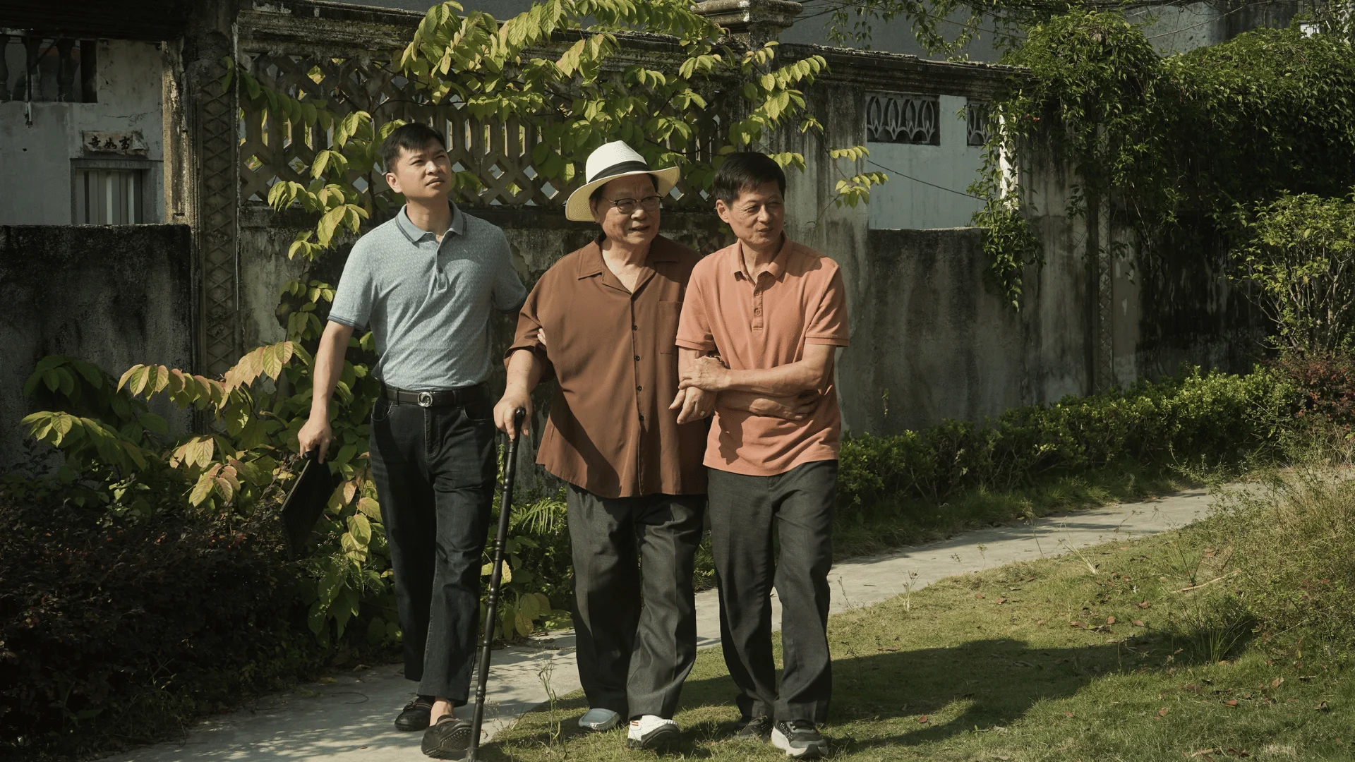 Three generations of men walk together through a sunlit garden in an official still from Dear You.