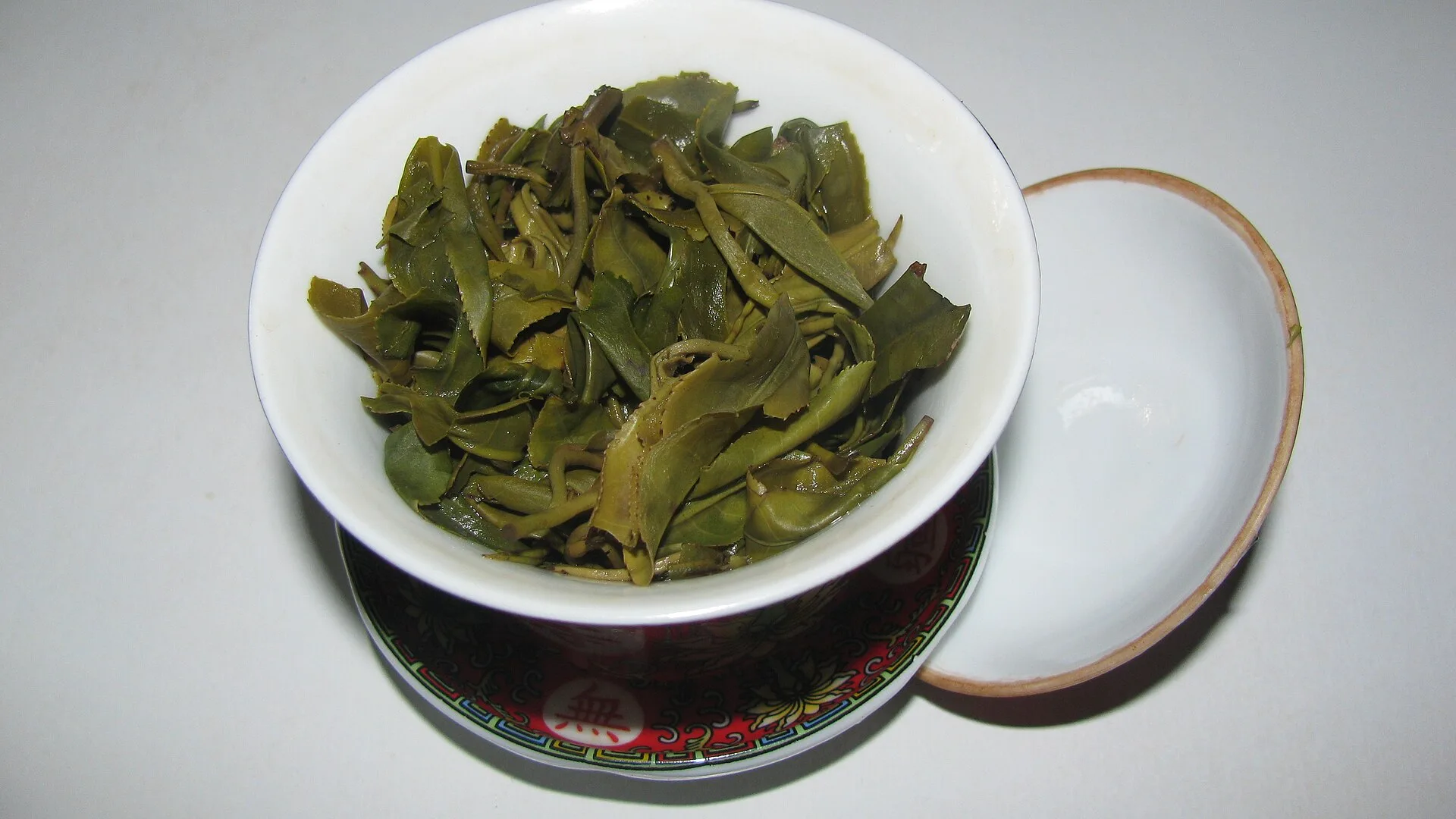 A porcelain gaiwan with its lid set to one side, revealing brewed Biluochun tea leaves inside the bowl.