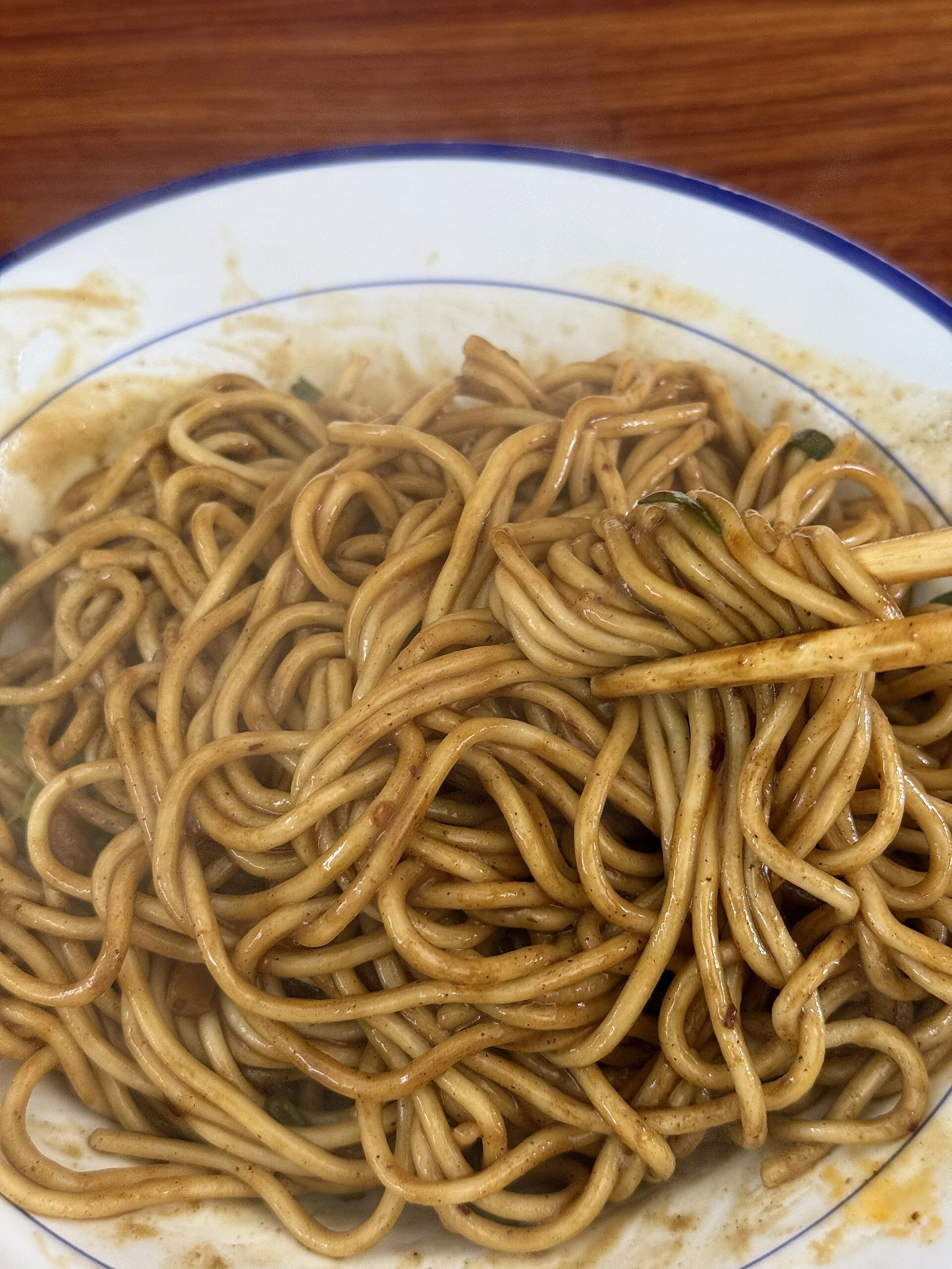 A close view of Wuhan hot dry noodles coated with sesame paste and topped with pickled vegetables.