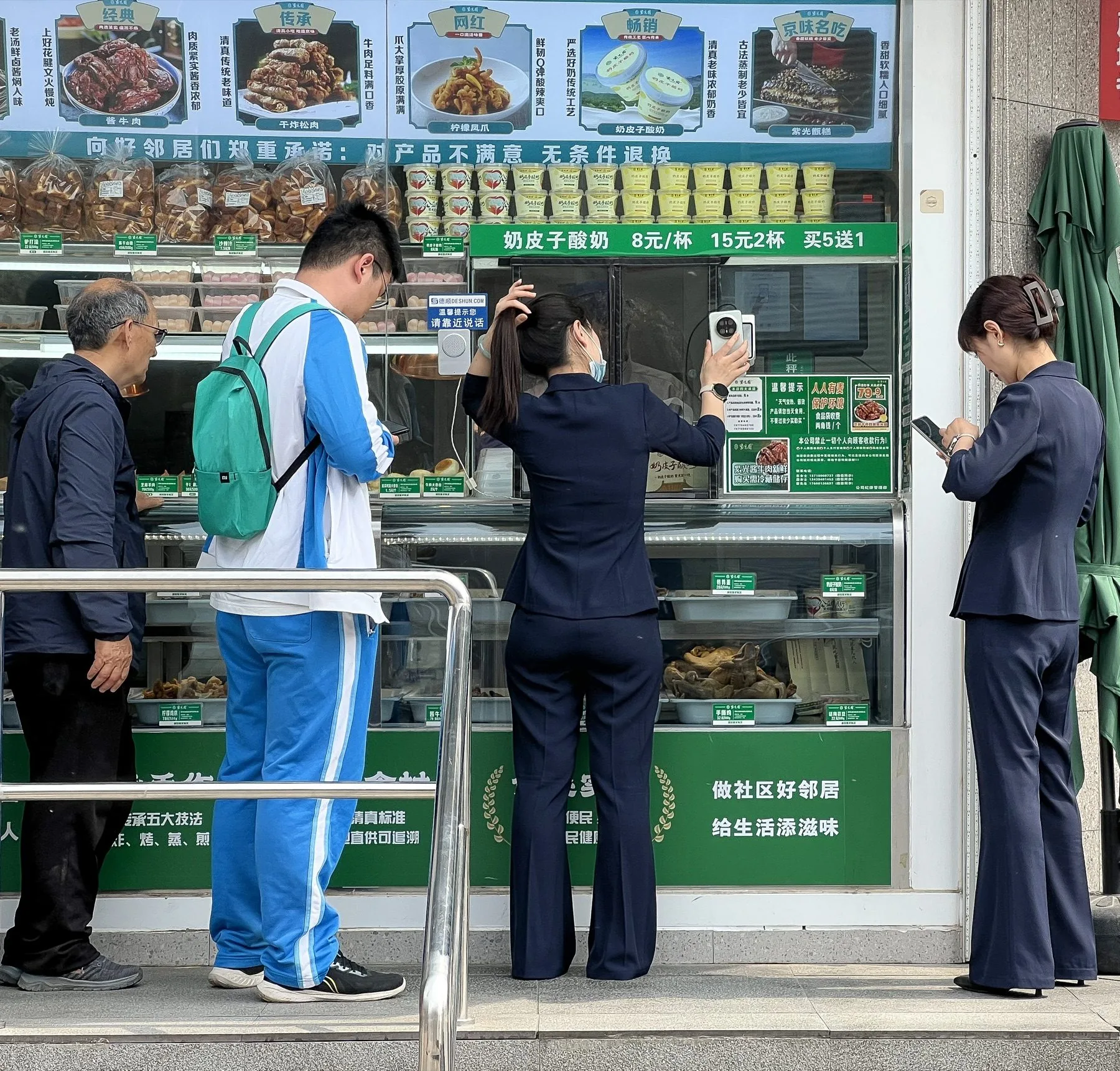 A customer at a Beijing restaurant window holds her phone's payment code toward the merchant's scanner while other customers wait.