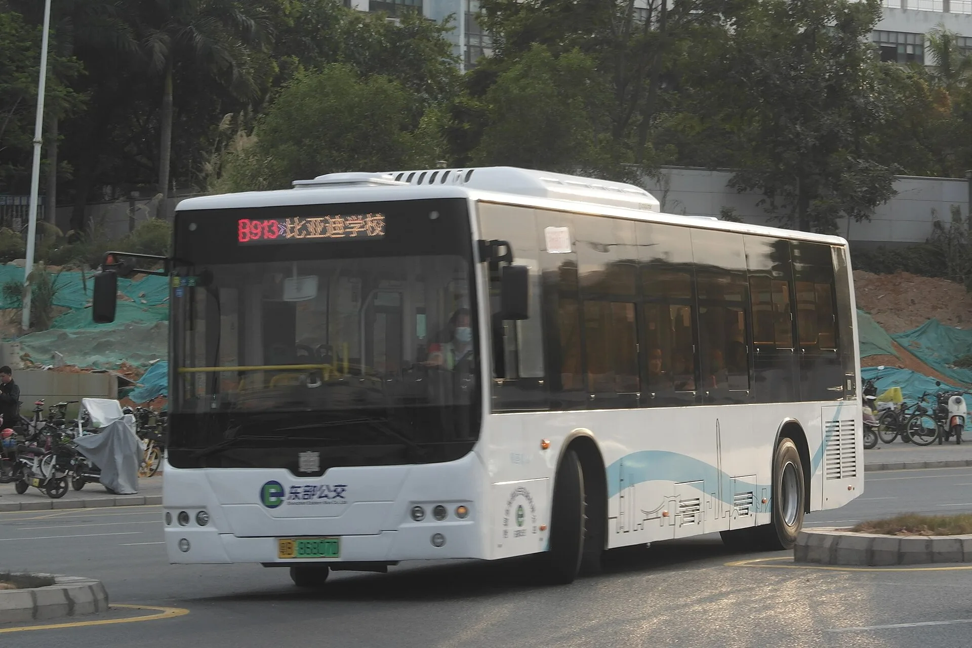 A white Shenzhen B913 electric city bus in service, with a green electric-vehicle licence plate and route display visible.