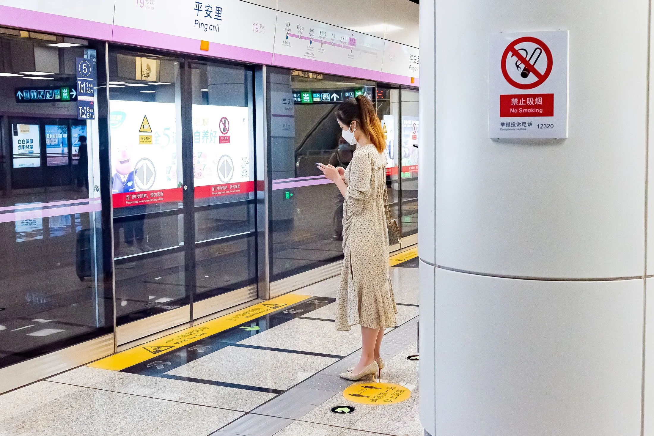 A passenger checks a smartphone while waiting behind platform doors at Ping'anli metro station in Beijing.