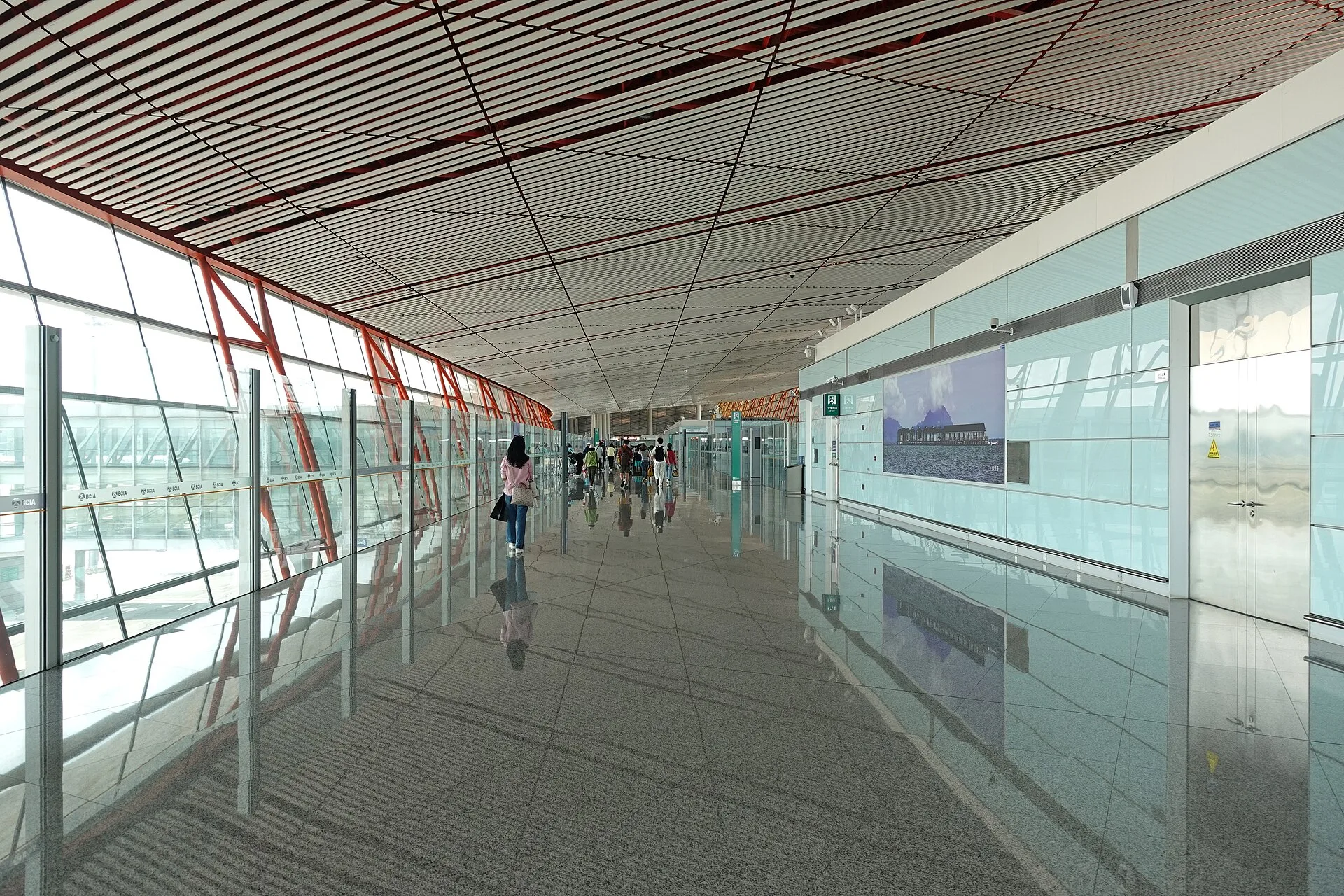 Travellers walk through the bright glass-sided international-arrival corridor of Beijing Capital Airport Terminal 3.