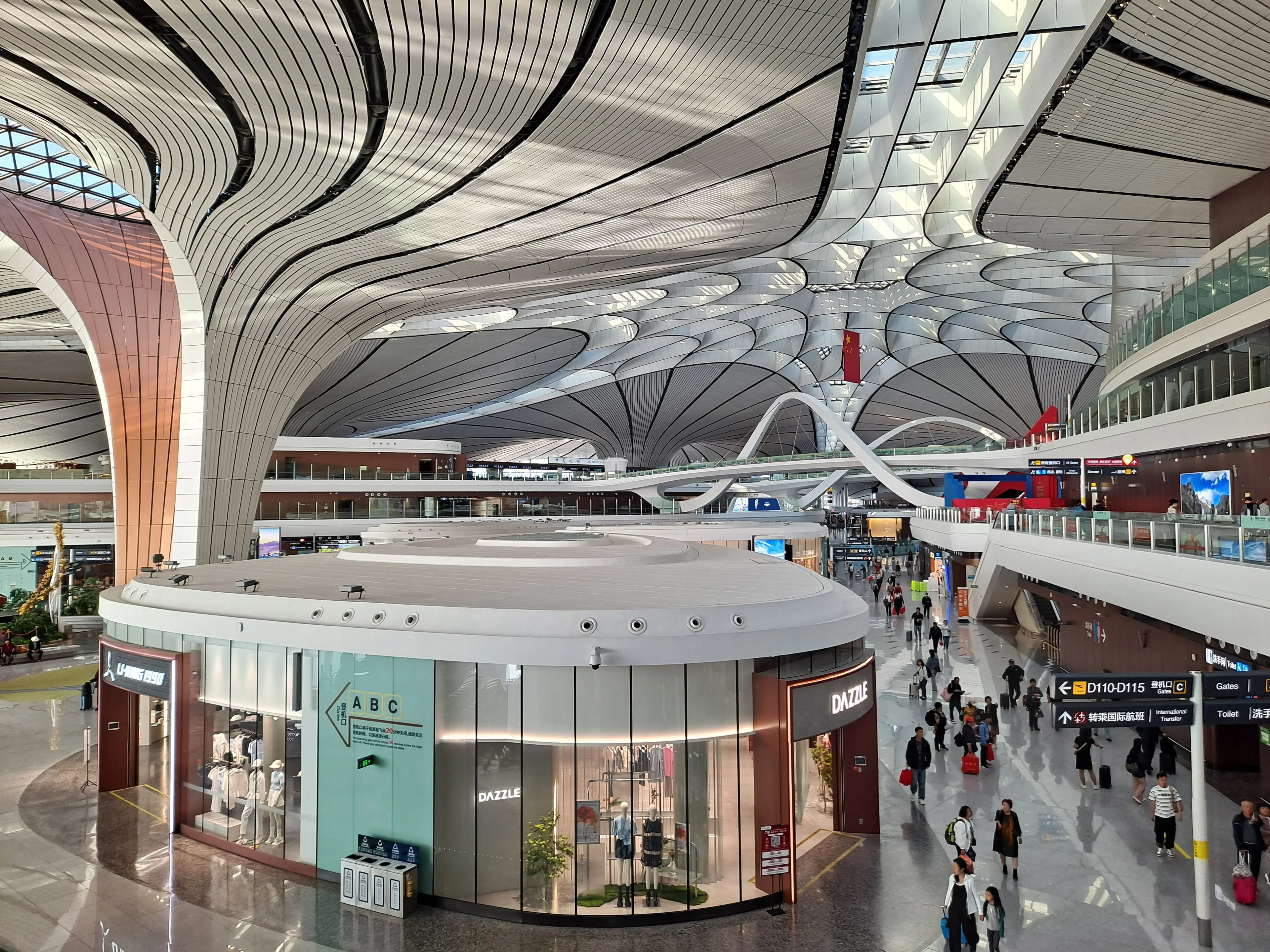 Travellers move through the vast curved central hall of Beijing Daxing International Airport beneath branching skylights.