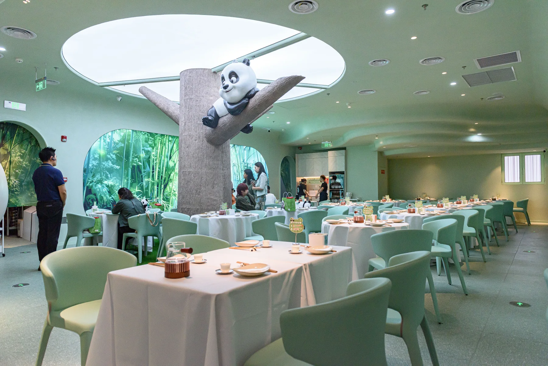 A bright contemporary restaurant interior in Beijing with white-clothed tables, green chairs and a large panda installation.