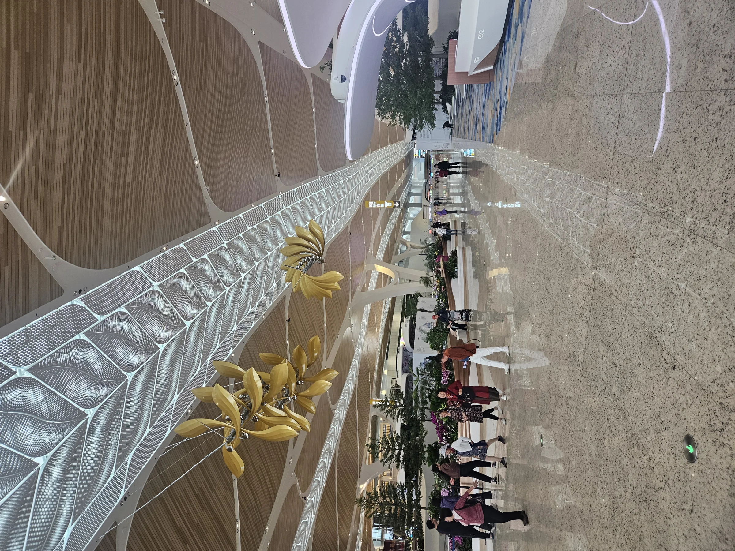 Travellers walk through Guangzhou Baiyun International Airport Terminal 3 beneath a leaf-patterned luminous ceiling and timber panels.