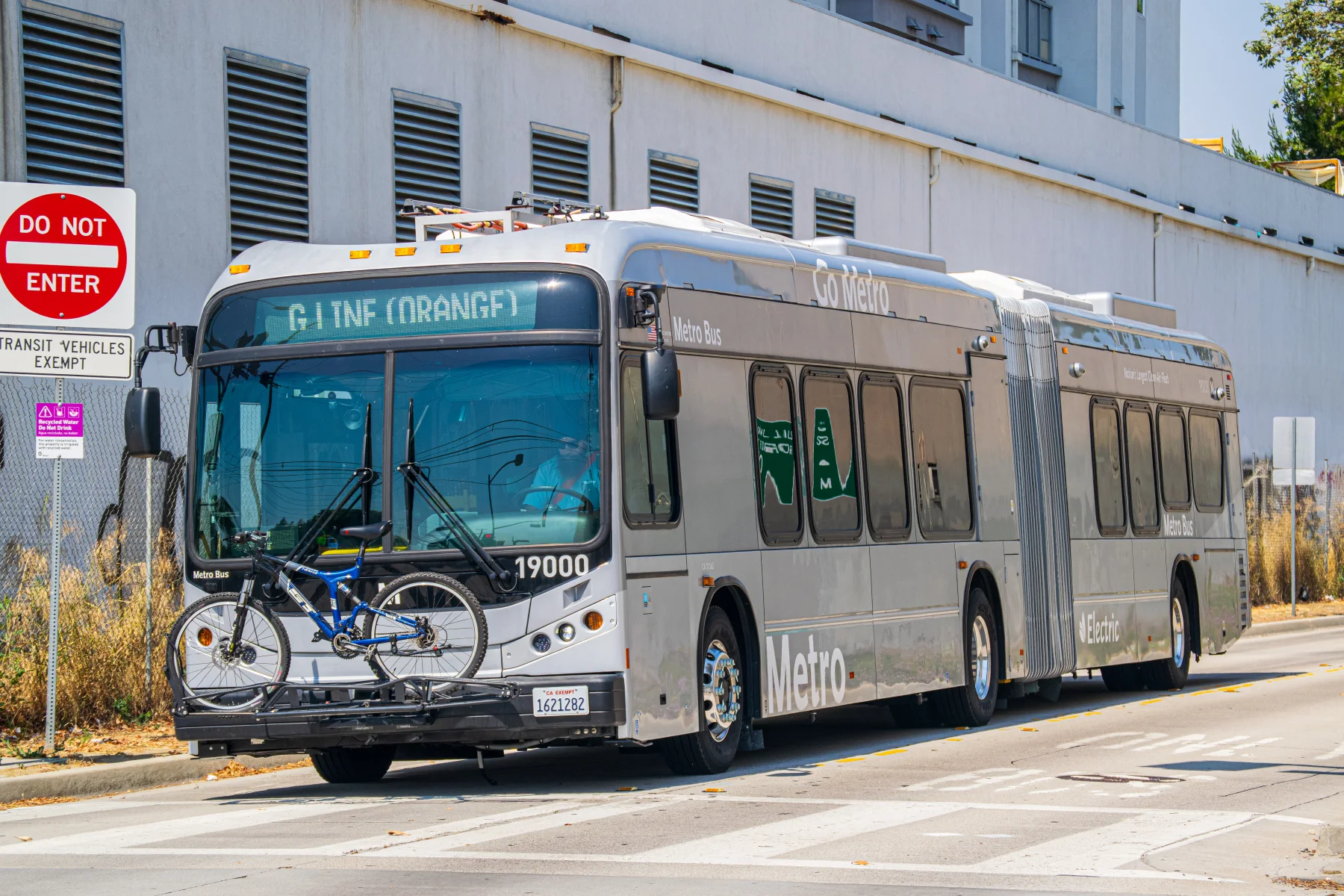 A silver articulated Los Angeles Metro G Line electric bus built by BYD travels in bright daylight in July 2024.