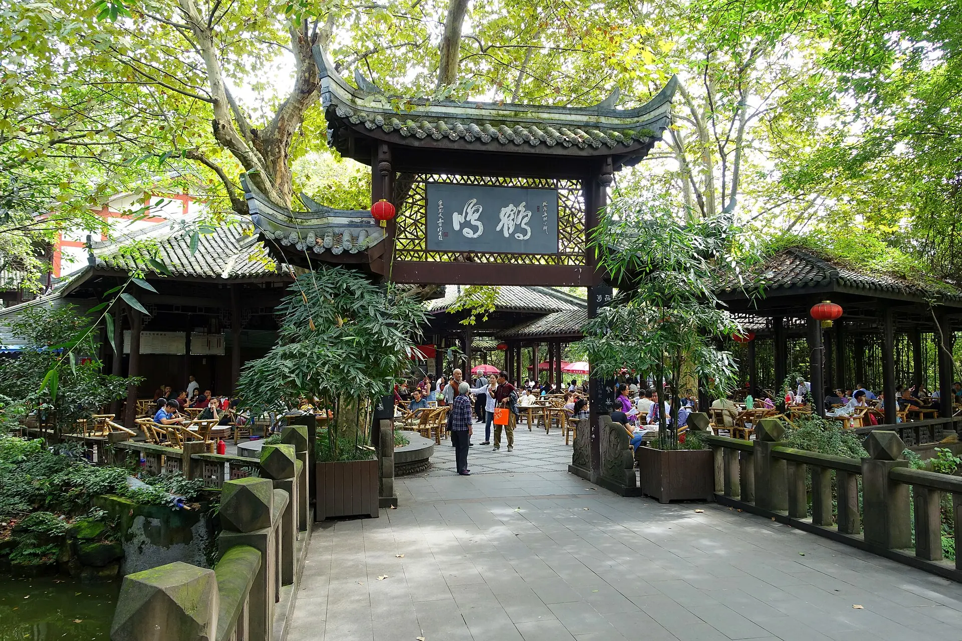 The open entrance to Heming Teahouse in Chengdu People's Park, with patrons seated at bamboo tables beneath trees.